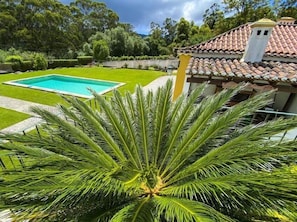 A swimming pool surrounded by a well-maintained lawn, with a house featuring a tiled roof in the background.