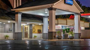 A 6 Office hotel entrance with a covered parking area, potted plants, and a visible number 6 on the building facade. - Motel 6 Byron, GA (Byron)