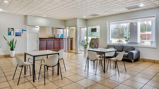 A spacious, well-lit room with a tiled floor, a dining area with a table and chairs, a sofa, and a large window offering a view of the outdoors. - Motel 6 Byron, GA (Byron)