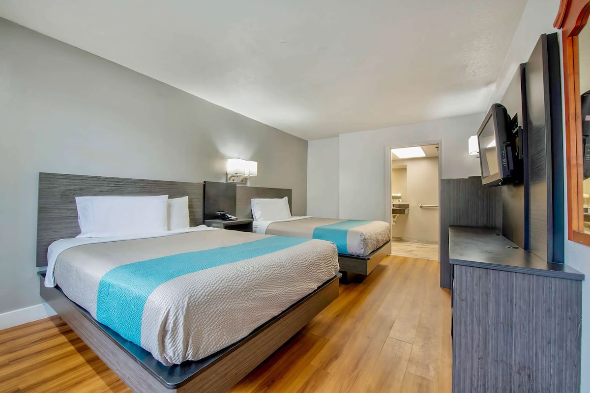 Ein Hotelzimmer mit zwei Betten, einem Fernseher, einem Schreibtisch und einem durchgegangenen Badezimmer.