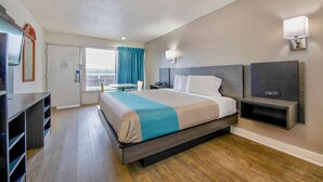 A hotel room with a bed, a desk, a TV, and a window with curtains. - Motel 6 Byron, GA (Byron)