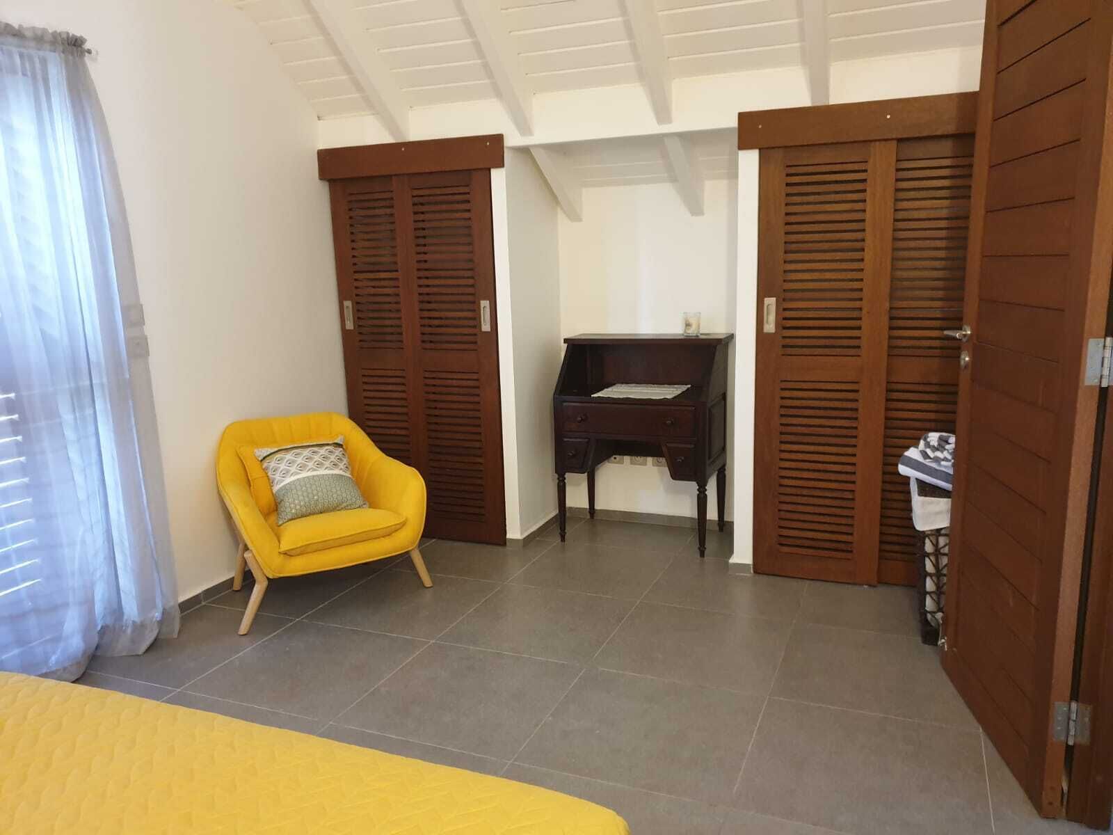 A room with a yellow bed, a yellow armchair, a desk, and wooden doors.