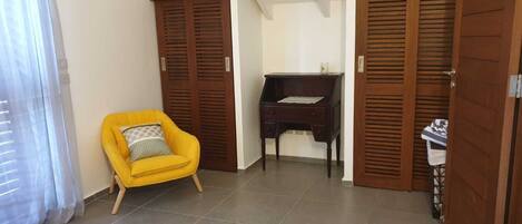 A room with a yellow bed, a yellow armchair, a desk, and wooden doors.