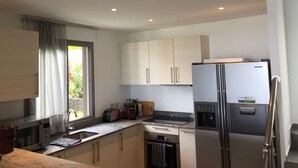 A modern kitchen with stainless steel appliances, a window with curtains, and light-colored cabinets.