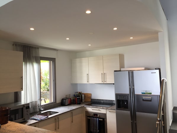 Una cocina moderna con electrodomésticos de acero inoxidable, una ventana con cortinas y armarios de tonos claros.