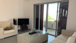 A modern living room with a sofa, a glass coffee table, and a flat-screen TV.