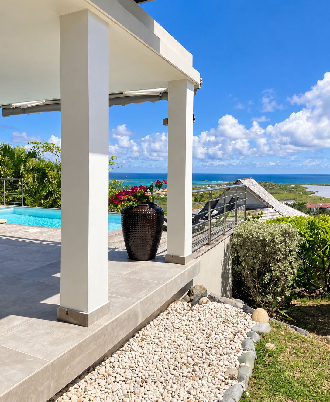 A covered outdoor area with a pool, a large planter with flowers, and a view of the ocean.