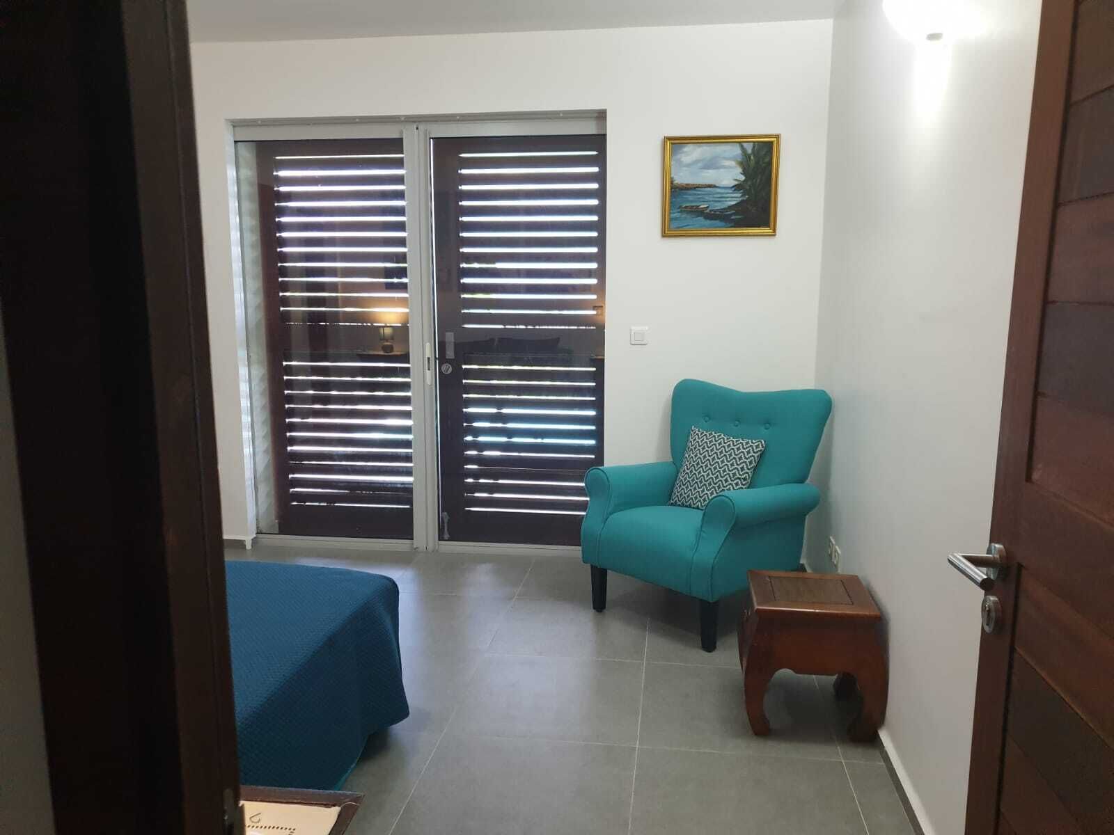 A room with a teal armchair, a small wooden side table, and a blue bedspread.