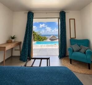A room with a bed, a desk, a chair, and a view of a swimming pool and ocean. - Air-Conditioned Villa with Pool and Ocean View in Orient Bay (Saint-Martin)