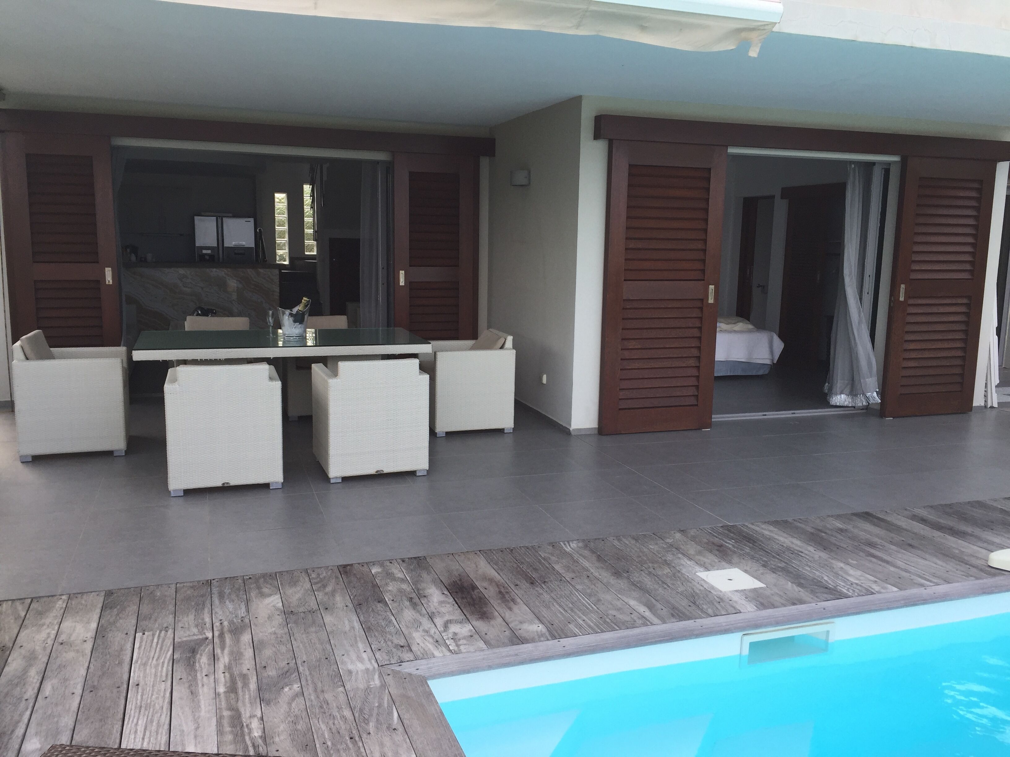 Un espacio exterior moderno con piscina, una mesa de comedor con sillas y acceso a un dormitorio.