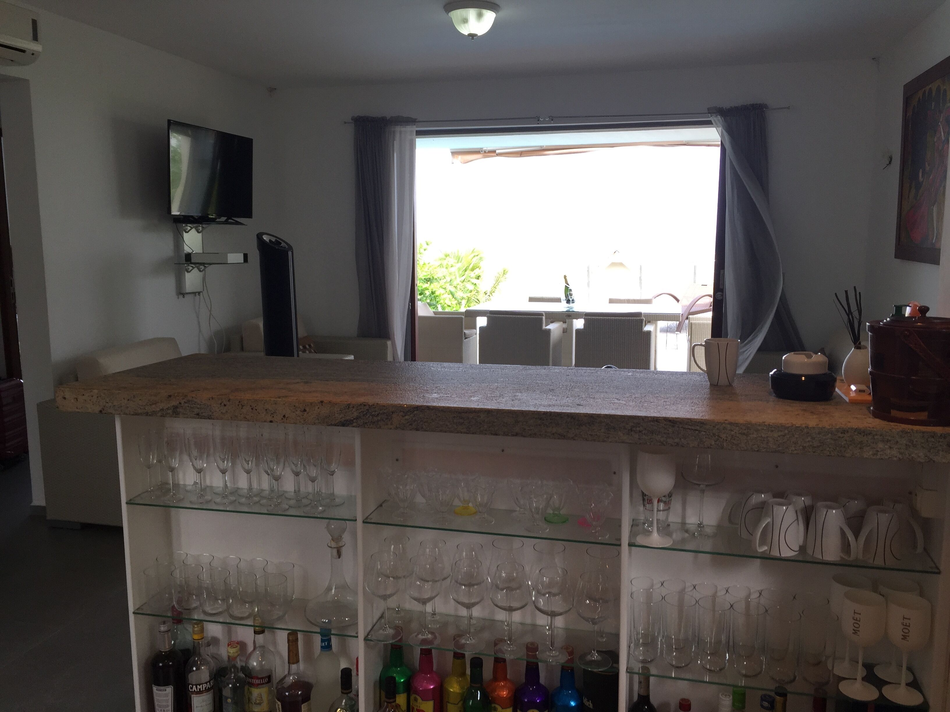 Zona de bar con mostrador, estantes con copas y botellas de vino, televisión y vistas al exterior.