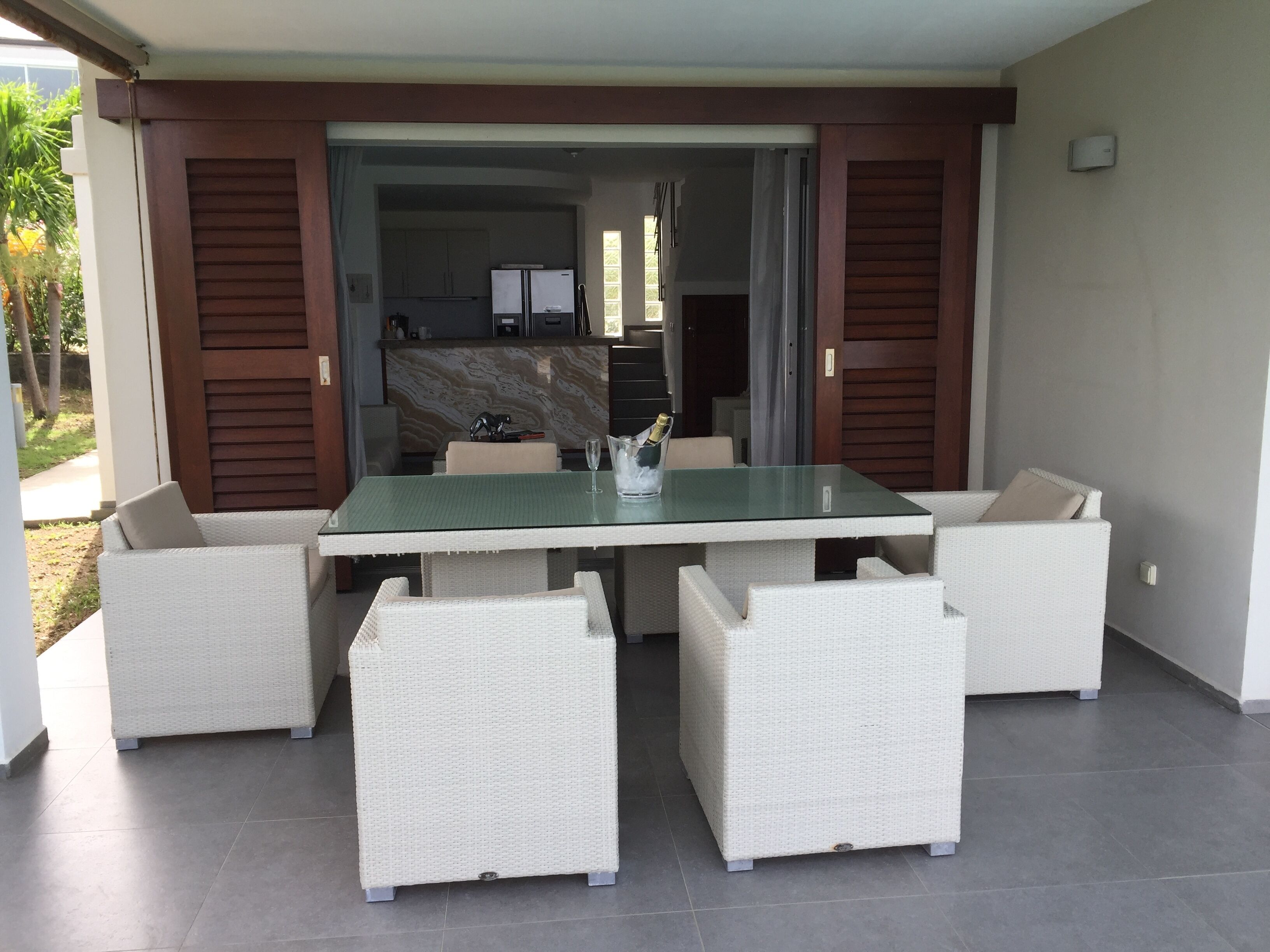 An outdoor patio with a glass-top table, surrounded by wicker chairs.