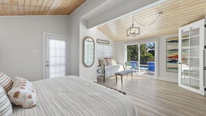A spacious bedroom with a large bed, a sitting area with a chair, a large mirror, and a view of the outside. - Private house with Pool and Spa! (Captiva)