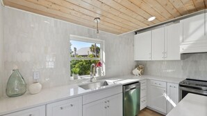 A modern kitchen with white cabinetry, a stainless steel dishwasher, and a window providing a view of greenery outside. - Private house with Pool and Spa! (Captiva)