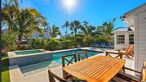 A pool area with a wooden table and chairs, surrounded by palm trees and a clear blue sky. - Private house with Pool and Spa! (Captiva)