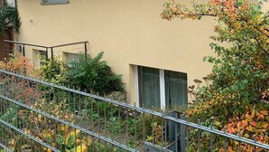 Ein zweistöckiges Gebäude mit sandfarbener Fassade, braunen Fensterläden und einer sichtbaren schwarzen Dachrinne.