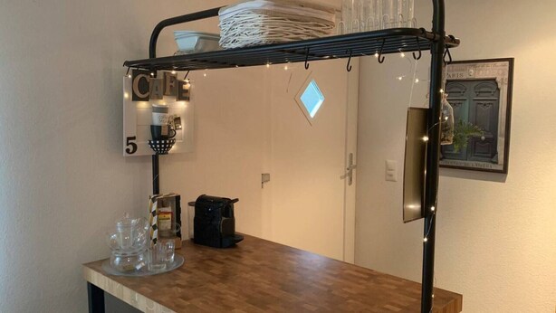 Eine Küchenzeile mit einer Kaffeemaschine, einem Glas und einem Kaffeekännchen auf einem Holztisch.