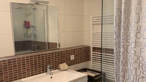 Ein Badezimmer mit weißem Waschtisch, einer Duschkabine aus Glas und einem gefliesten Boden.