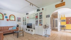 Una sala de estar con un sofá, televisor y armarios. Hay un ventilador y un cartel en la pared.