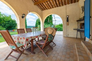 Eine Terrass mit Tisch, Stühlen, einem Grill und Blick ins Grüne.