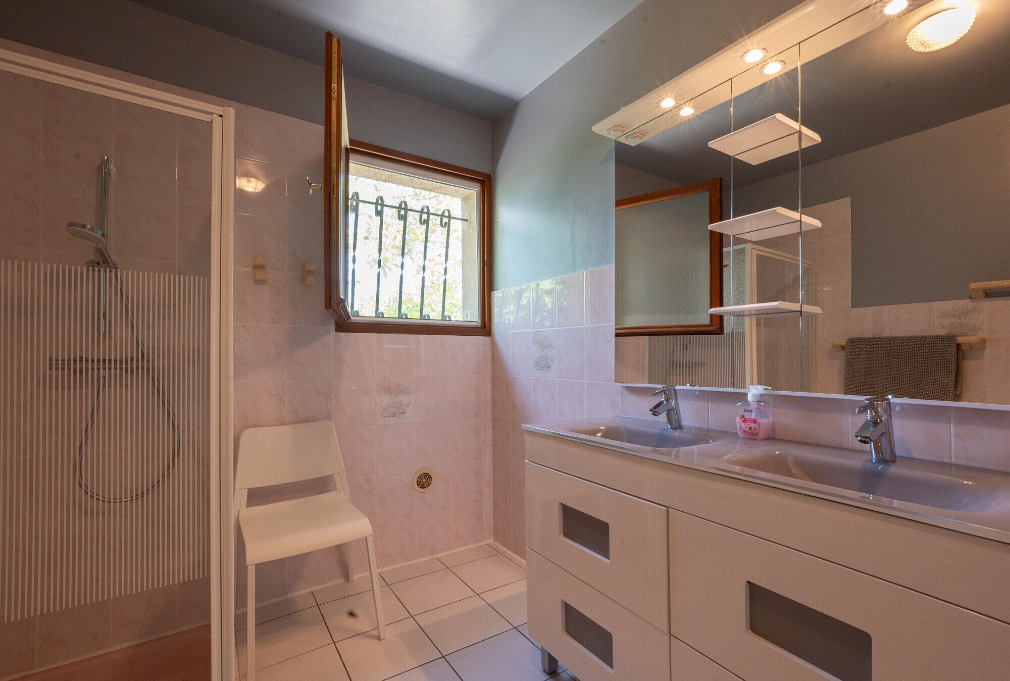 Une salle de bain avec une douche, un lavabo, un miroir et une fenêtre.