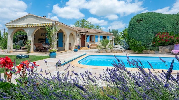 Una villa de estilo mediterráneo con piscina, mobiliario de exterior y exuberante vegetación.