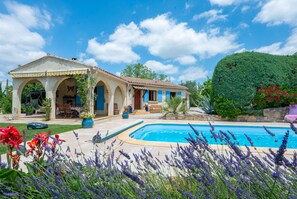 Una villa de estilo mediterráneo con piscina, mobiliario de exterior y exuberante vegetación.