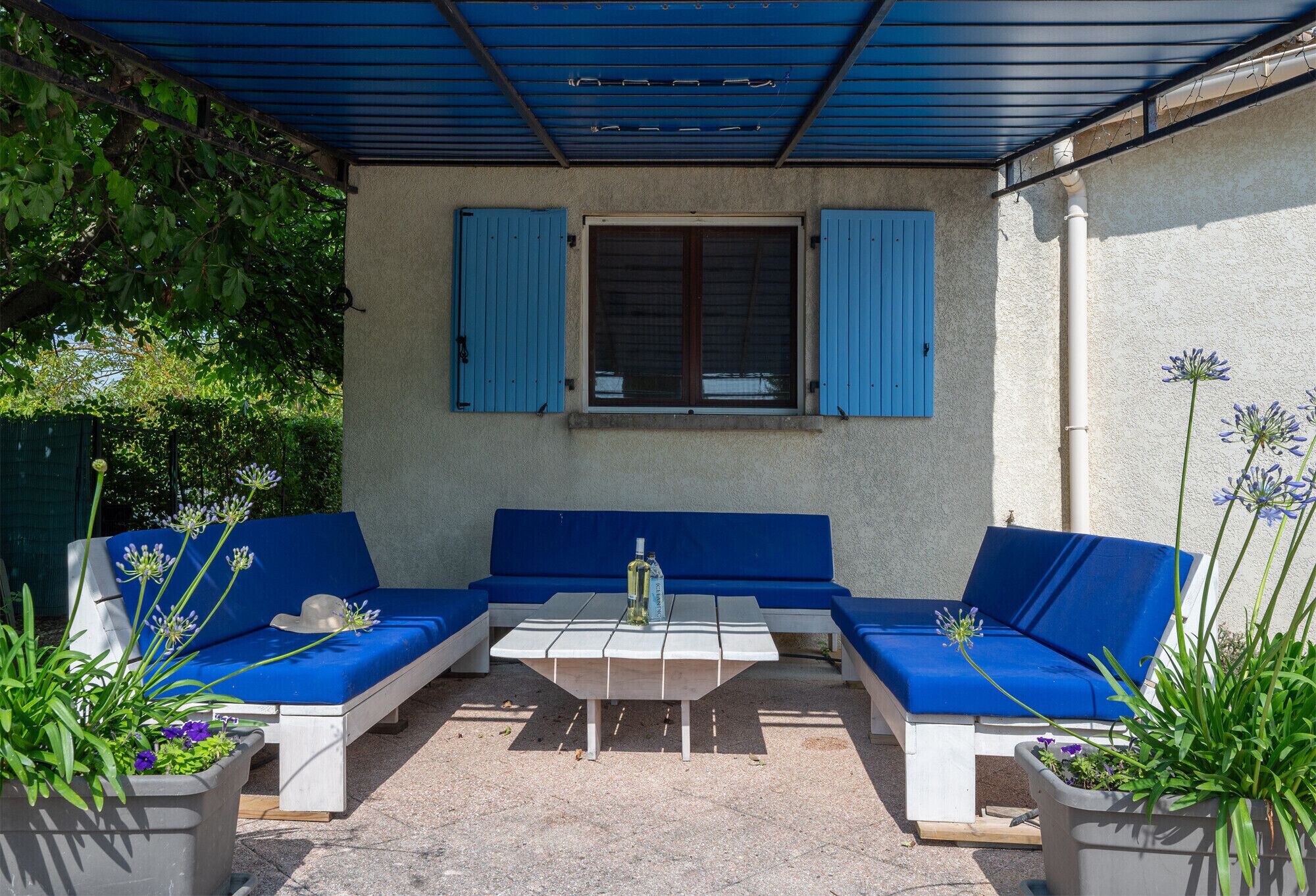 A covered outdoor seating area with a table, blue cushions, and potted plants.