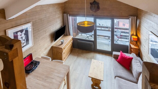 Une pièce chaleureuse avec un décor intérieur en bois, un canapé, une table avec un tourne-disque, une télévision et une grande fenêtre donnant sur l’extérieur.