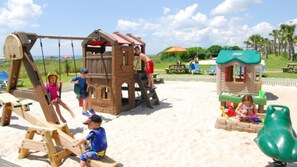 A children's play area with a swing set, climbing structures, and a small house.