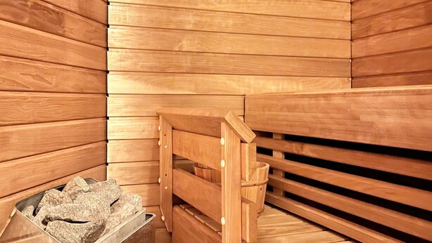 Una sauna con listones de madera, un banco y una piedra para lavarse.