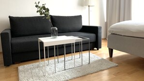 Una sala de estar moderna con un sofá gris oscuro, una mesita auxiliar blanca con patas metálicas, una alfombra blanca y una lámpara de pie.