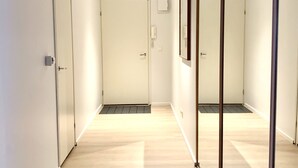 Un pasillo con paredes espejadas, puertas blancas y suelo de madera clara.