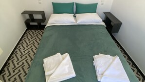 Ein ordentlich gemachtes Bett mit grüner Bettwäsche und weißen Kissen, ein Bild an der Wand und ein gemusterter Boden.