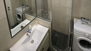 Ein modernes Badezimmer mit einer gläsernen Duschkabine, einer integrierten Waschmaschine und einem großen Spiegel.