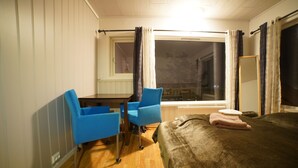 Una habitación de hotel con una cama, dos sillas azules, una mesita y una ventana con cortinas.