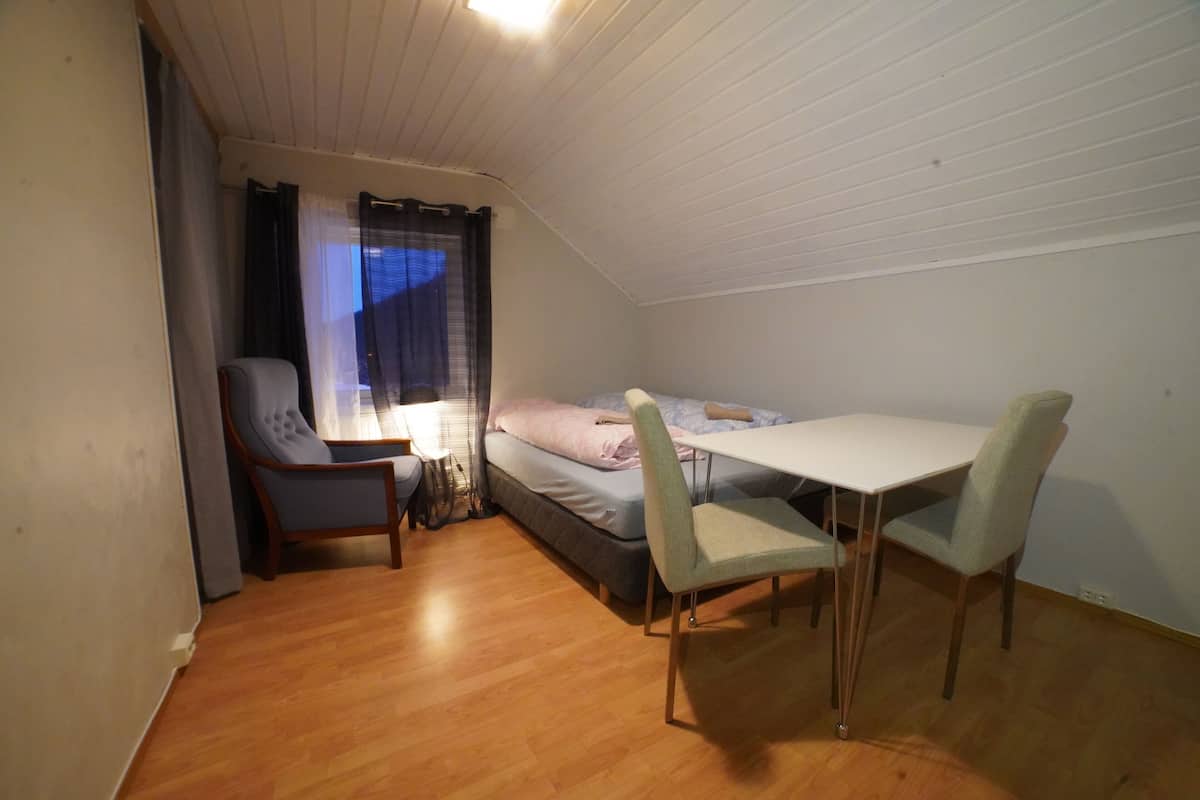 Um quarto pequeno e acolhedor, com uma cama, uma escrivaninha e duas cadeiras.