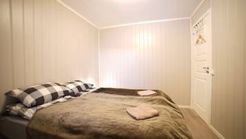 Quarto com cama, almofadas, uma porta e luminária fixada na parede.