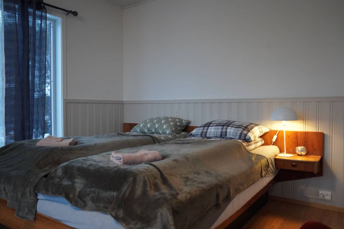 Uma cama de casal com cabeceira de madeira, uma mesa de cabeceira com abajur e uma janela com cortinas.