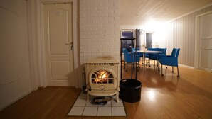Una habitación con chimenea de ladrillo blanco, una mesa de comedor con sillas azules y un cubo negro cerca de la chimenea.