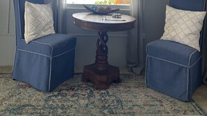 Une pièce avec deux fauteuils bleus, une petite table en bois et une fenêtre donnant sur l’océan.