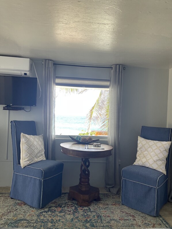 A room with two blue armchairs, a small wooden table, and a window with a view of the ocean.