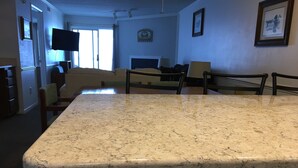 Een keuken met een marmeren aanrecht, houten stoelen, een eettafel en een aan de muur bevestigde televisie.