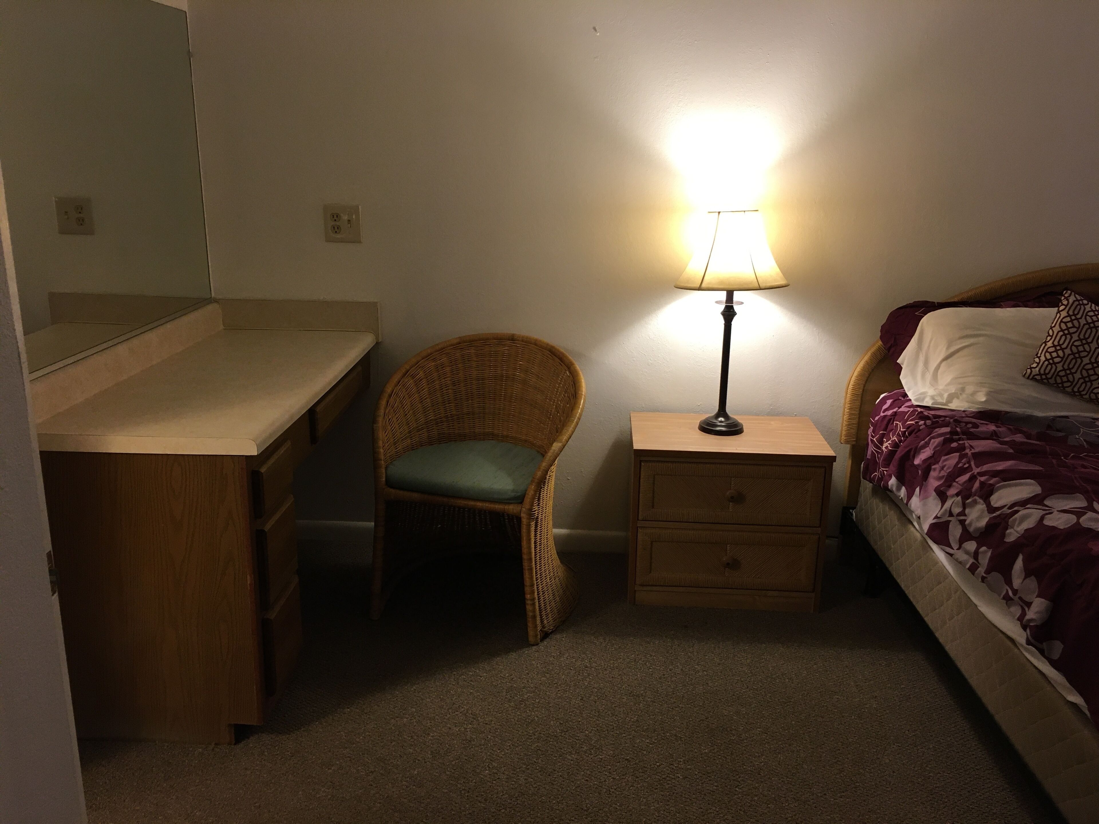 Una camera da letto con un letto, una sedia, una scrivania e un comodino con una lampada.
