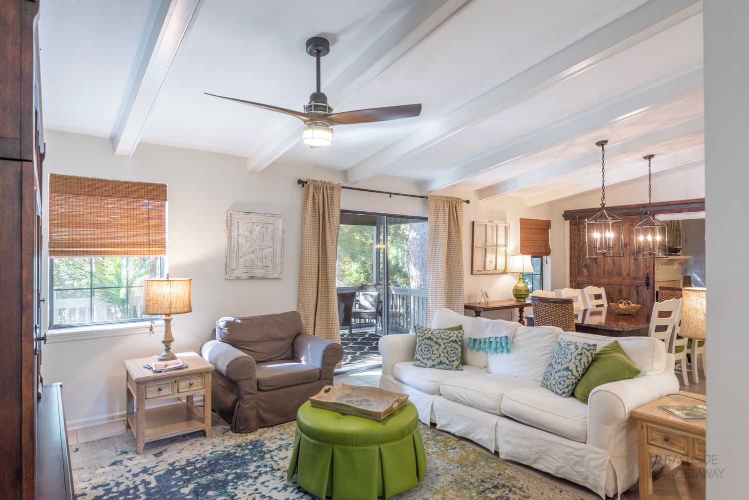 A spacious living room with a ceiling fan, a green ottoman, a white sofa, and a dining area with wooden chairs and a table.