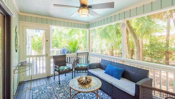Eine überdachte Veranda mit Deckenventilator, einer Couch mit blauen Kissen und einem kleinen Tisch mit dekorativer Tischdekoration.