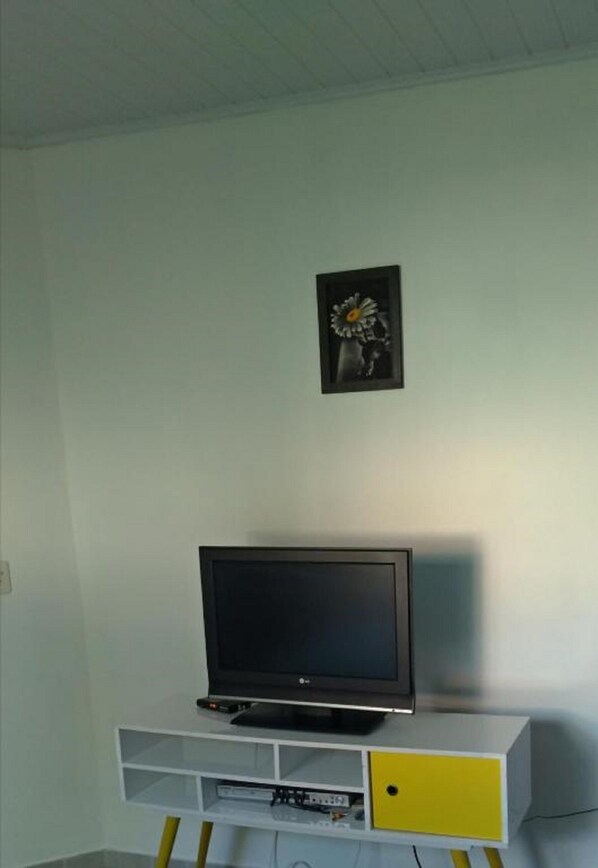 A television on a white and yellow TV stand with a picture frame above it.