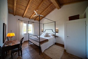 Ein Bett mit Baldachin, ein weißes Bettgestell, eine Holztisch mit Lampe, ein Sessel, ein weißer Kleiderschrank und ein Deckenventilator.