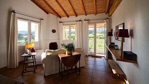A cozy room with a wooden ceiling, a dining table, a sofa, and a view of a vineyard through the windows. - Beautiful cottage with stunning views and pool (Vinza) (Galtelli)