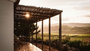 Ein möblierter Patio-Bereich mit einer Pergola, Steinsitzgelegenheiten und Blick auf sanfte Hügel in der Ferne.